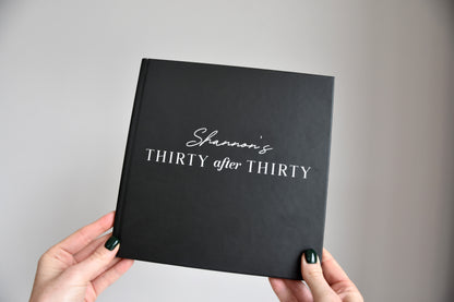 Elegant 21cm x 21cm black notebook with minimalist design titles 'Shannon's Thirty after Thirty' held by hands against a gray background