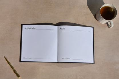 Open notebook with pages numbered 29 and 30, next to a pen and a cup of tea on a beige surface.