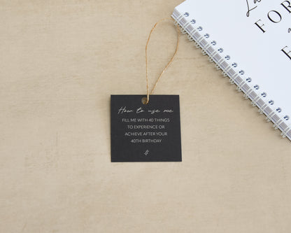 Black square tag with text on a beige surface next to a white notebook.