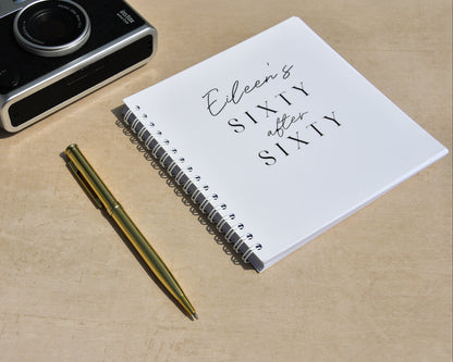 Notebook with 'Eileen's Sixty after Sixty' text, pen, and camera on a wooden surface