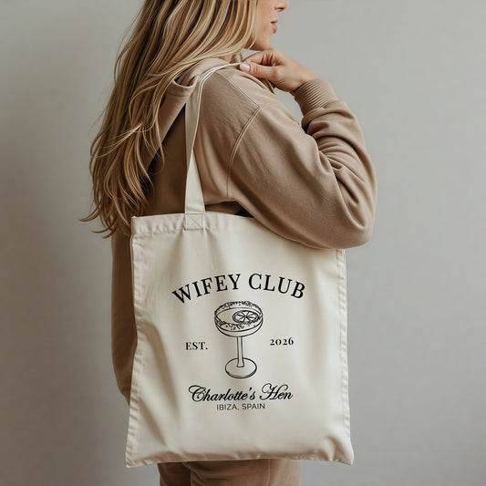Person holding a tote bag with 'Wifey Club' text and design.