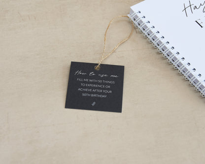 Black tag with text on a beige surface next to a notebook