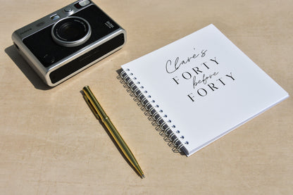 Camera, personalised 40 before 40 notebook with text, and pen on a beige surface